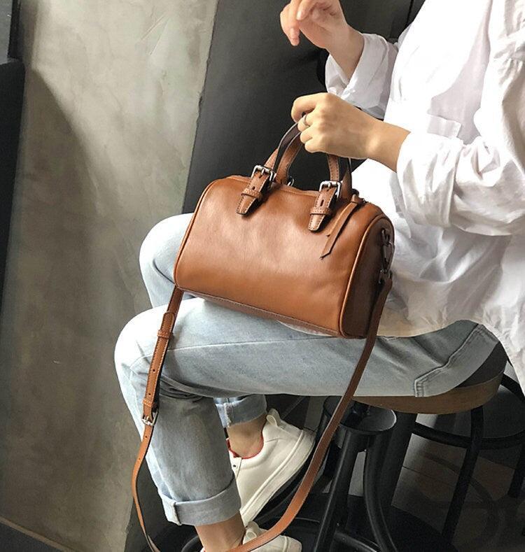Small vintage leather Boston bag with top handles and crossbody strap, worn by a woman