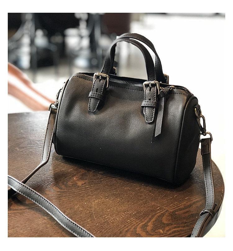 Small black vintage leather Boston bag with top handles and crossbody strap on a wooden table