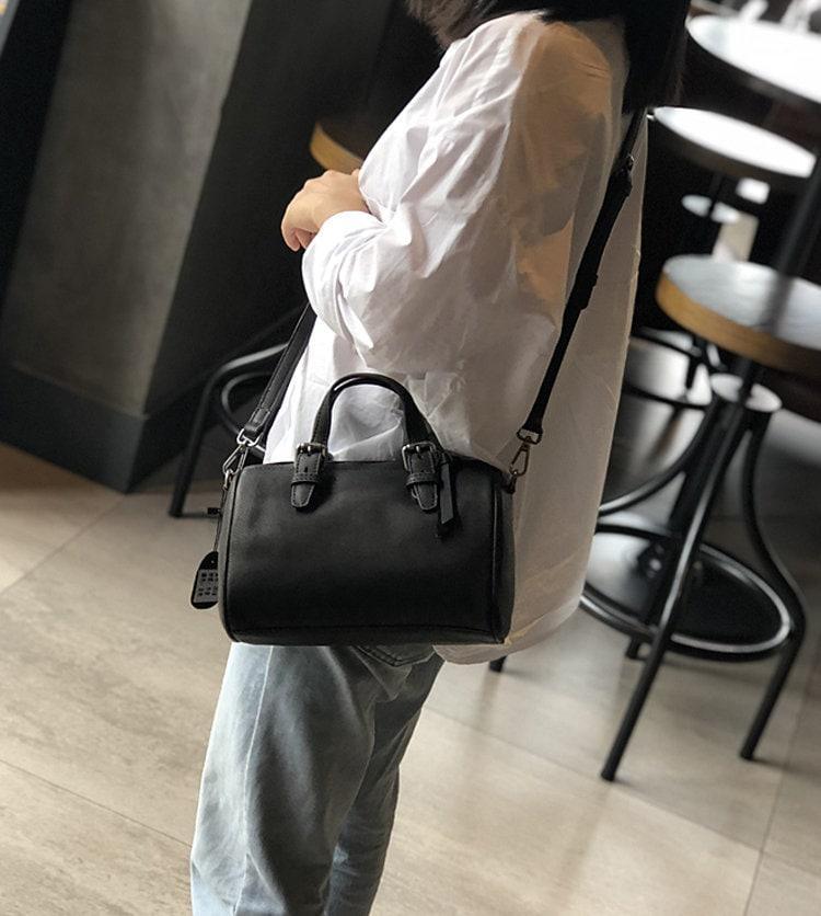Woman wearing a small vintage black leather Boston bag with crossbody strap and top handles
