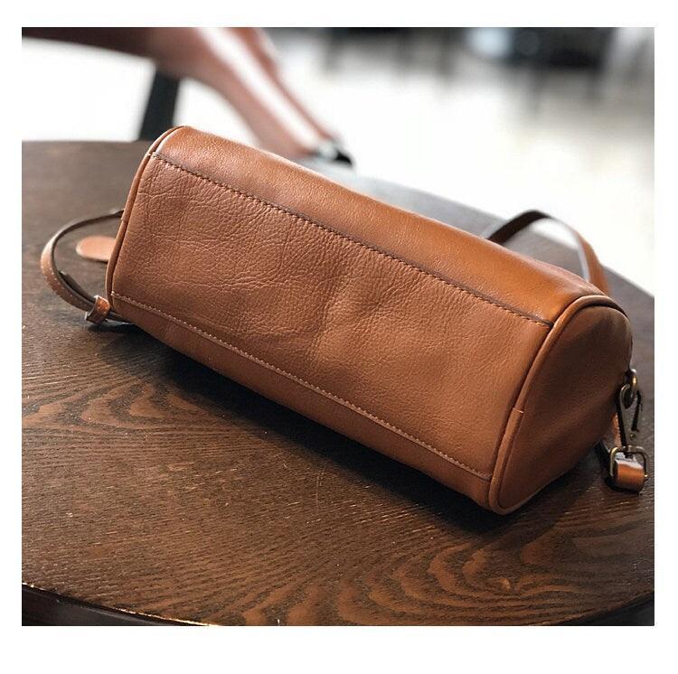 Small vintage brown leather Boston bag with crossbody strap on a wooden table