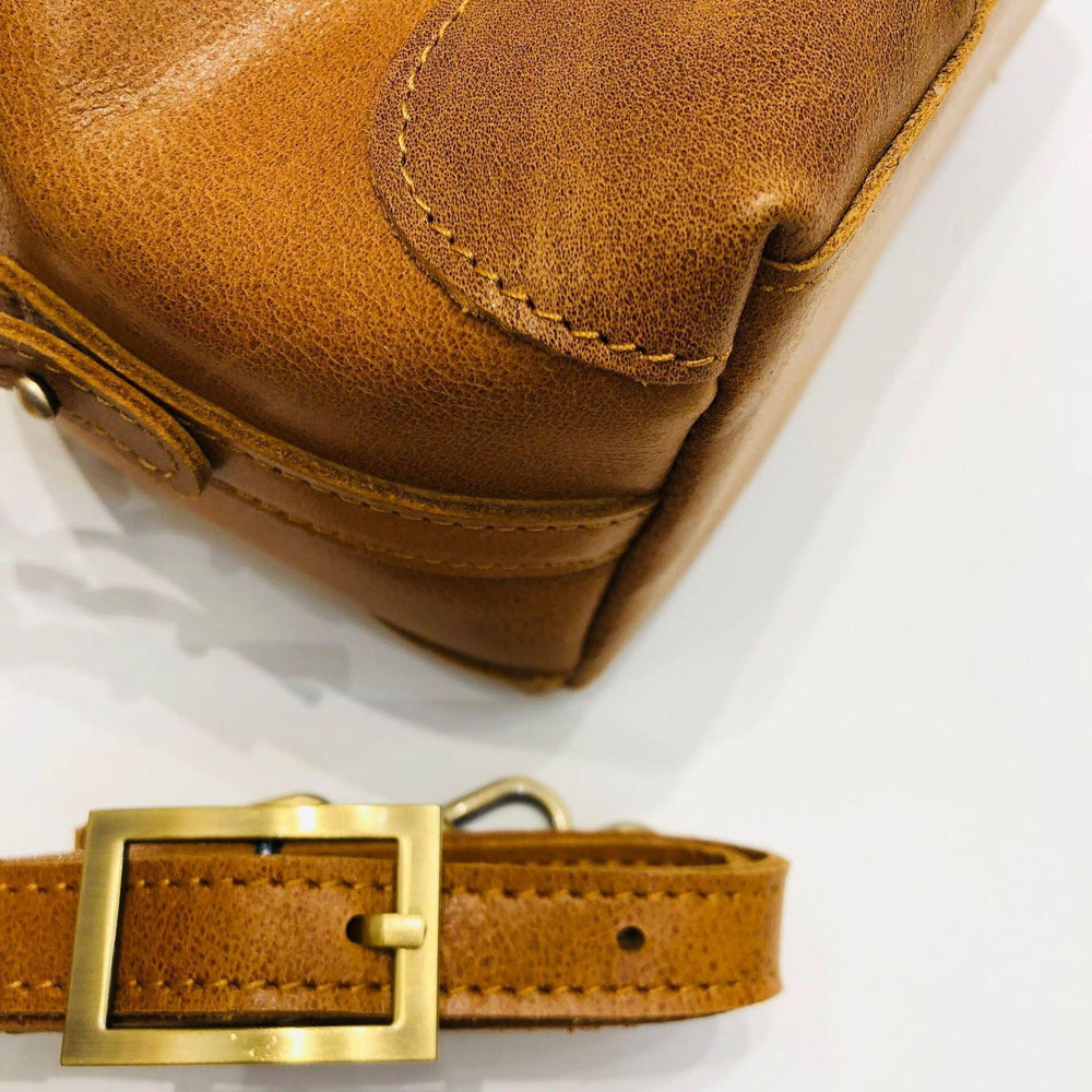Close-up of brown vintage leather crossbody bag with gold buckle and visible stitching
