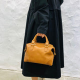Woman holding a vintage tan leather Boston bag with top handles against a white wall background