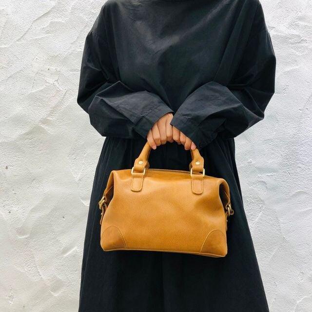 Woman holding vintage tan leather Boston bag with top handles against a white wall