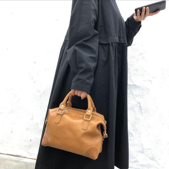 Woman in black dress holding tan vintage leather Boston bag with top handles